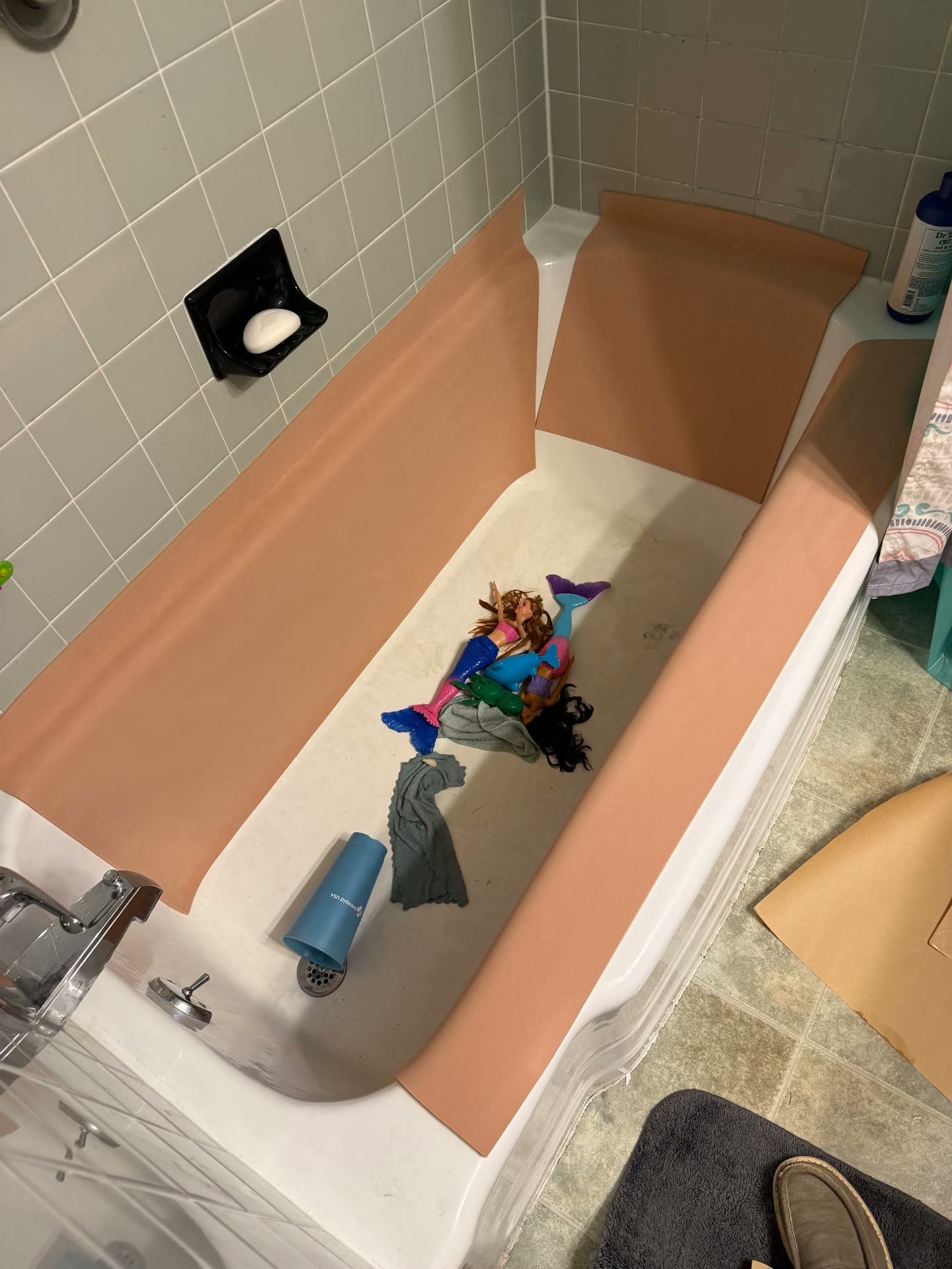 A home bathtub lined with peach foam panels along both sides and the back wall, with bath toys and a cup resting on the open bathing floor.