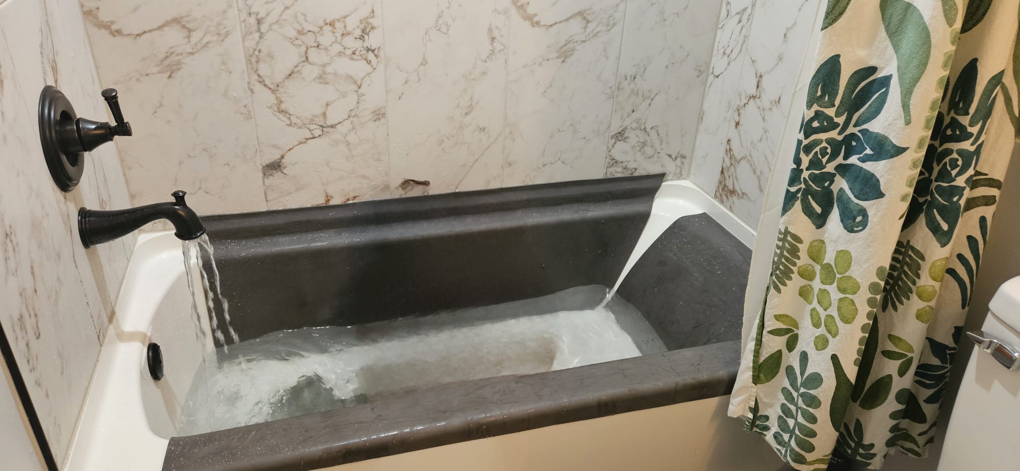 Water running into a bathtub with the dark grey kit fitted along the back wall, both sides, and the front tub edge.