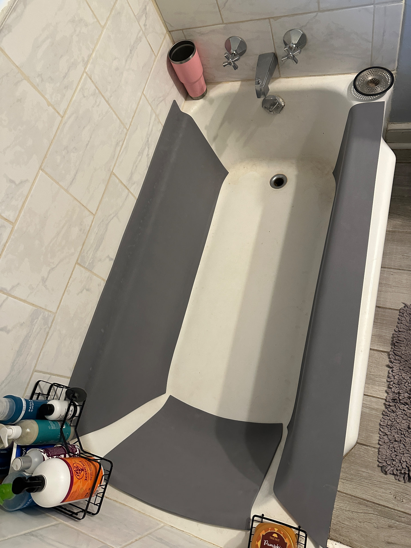 An empty bathtub with grey foam panels fitted along both side walls, the back wall, and the front tub edge, with a shower caddy beside it.