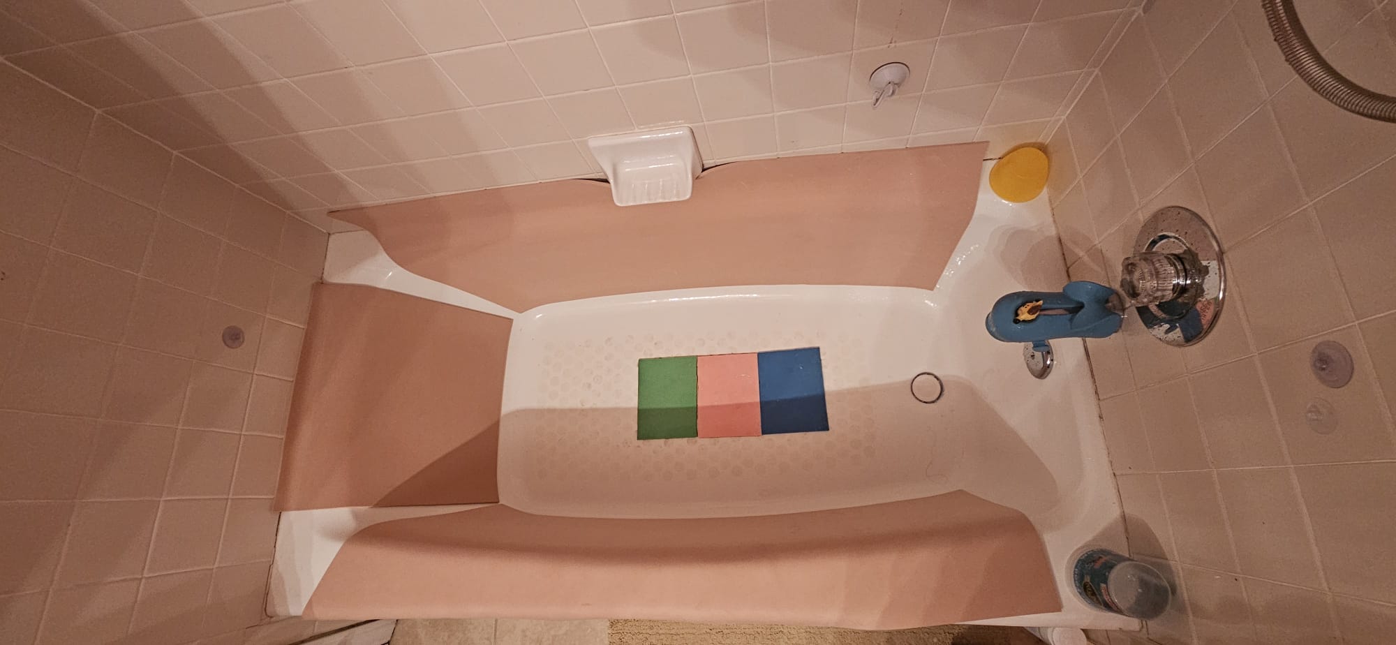 Overhead view of a bathtub lined with peach foam panels along both sides and the back wall, with three colored foam squares resting on the tub floor.